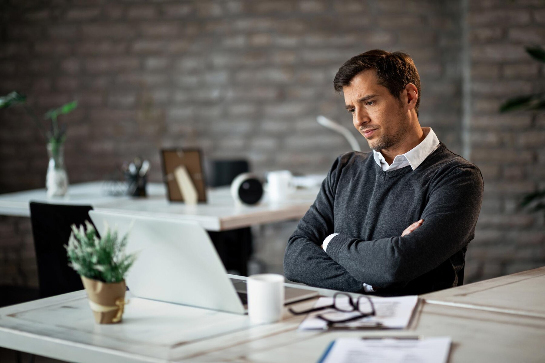 Businessman with arms crossed reading an email on laptop at work
