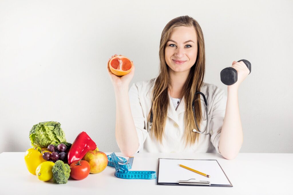 Female dietician holding grapefruit and dumbbell in clinic