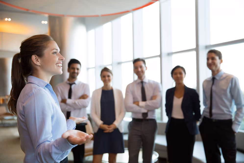 A group of six professionals engaged in a discussion in a modern office environment, with large windows and a collaborative atmosphere.