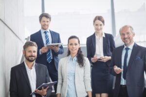 A group of five professionals in business attire, standing and engaging in conversation in a modern office environment.