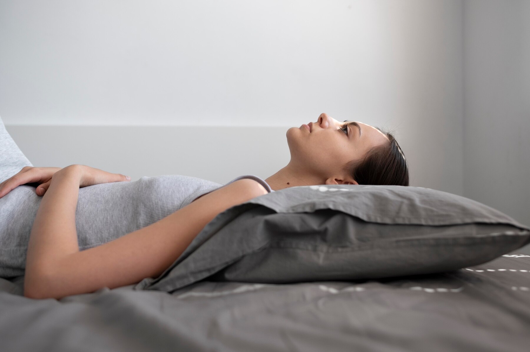 A young woman lying on her back in bed, peacefully staring upwards, in a room with soft natural light.