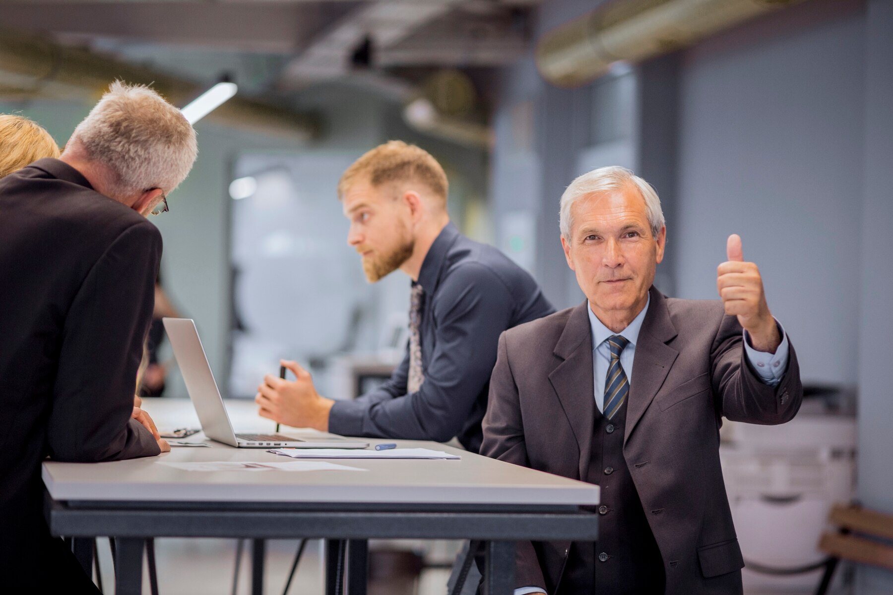 A group of professionals engaged in discussion around a table; one person gives a thumbs-up, indicating approval or success.
