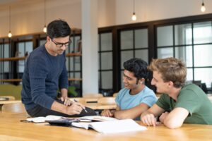 Three men discussing notes at a table in a modern office space.