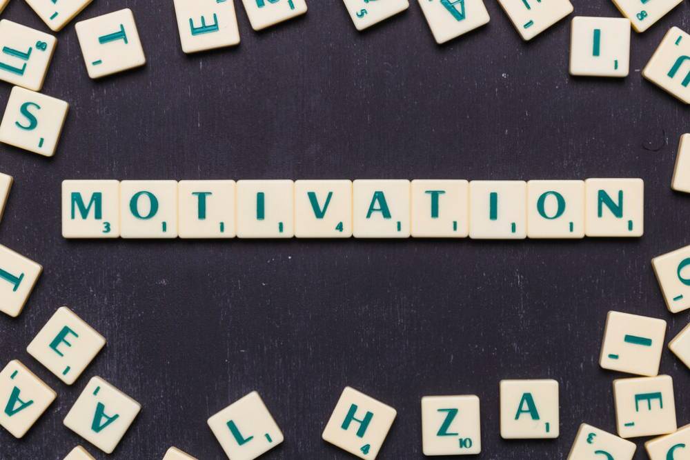 A collection of Scrabble tiles surrounding the word 'MOTIVATION' displayed prominently in the center on a dark background.