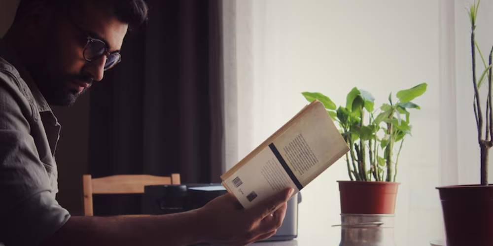 A person reading a book in a cozy room with sunlight filtering through the window.