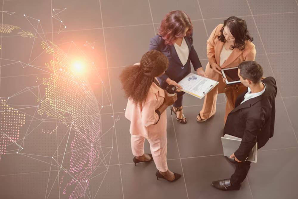 Four professionals in business attire discussing a document, with a digital world map overlay in the background.