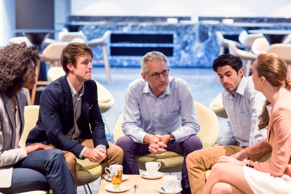 A group of five people sit in a modern cafe setting, engaged in conversation.